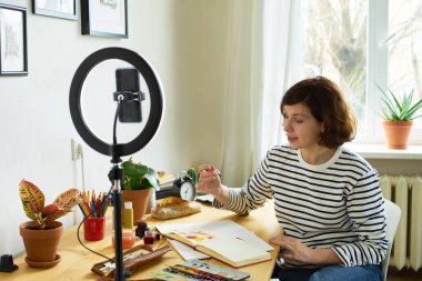 Online eğitim için evde tasarım atölyesi çeken kadın sanatçı. Halka ışıklarını kullanarak ev yapımı yüksek lisans yapıyorum. Samimi sanatçının stüdyosu. 
