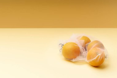 Tekrar kullanılabilir poşetlerle sıfır atık yiyecek alışverişi. Tekstil ambalajında meyvelerle yatıyordu. Sarı arkaplanda portakallar.