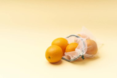 Tekrar kullanılabilir poşetlerle sıfır atık yiyecek alışverişi. Tekstil ambalajında meyvelerle yatıyordu. Sarı arkaplanda portakallar.