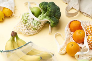 Tekrar kullanılabilir poşetlerle sıfır atık yiyecek alışverişi. Tekstil ambalajında meyve ve sebzelerle yatıyordu. Sarı arka planda muz, brokoli, turp ve portakal..