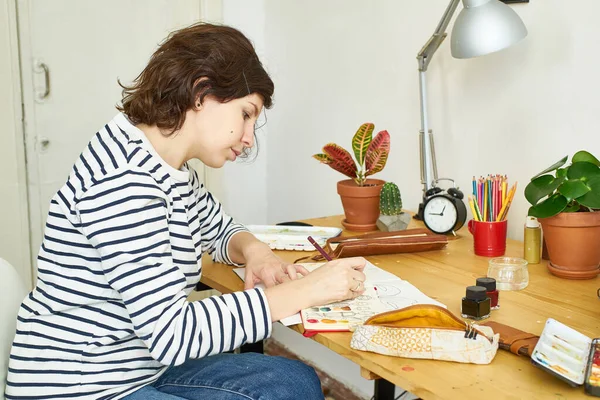 예술가 집에서 일하고 있습니다 청바지와 셔츠를 여자가 테이블에 그림을 그리는 — 스톡 사진