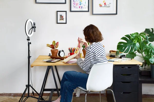 Female artist filming design workshop at home for online education. Working from home making master-class using ring lighting. Cozy artist\'s studio.