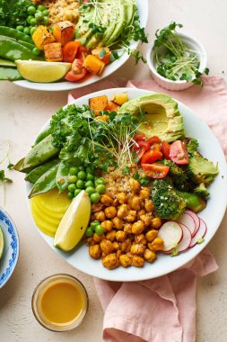 Avokado ve nohutlu sağlıklı vejetaryen yemek kaseleri kinoalı nohut ve mikro yeşillikle süslenmiş sebzeler ve taş zeminde fındık sosu.