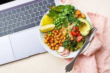 Laptop ve avokado ile sağlıklı vejetaryen yemek kasesi ve kinoalı nohut ve mikro yeşillik ve fındık sosuyla süslenmiş sebzeler. İş konsepti için iyi yemek.. 