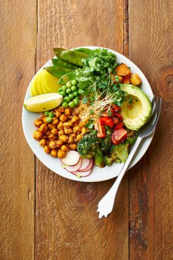 Avokado ve nohutlu sağlıklı vejetaryen yemek kasesi. Kinoalı ve sebzeli. Mikroyeşillik ve ahşap arka planda fındık sosu.