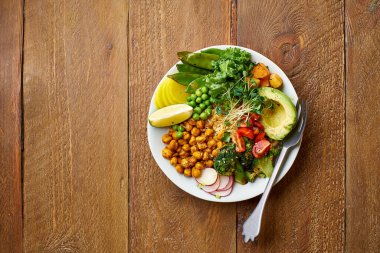 Avokado ve nohutlu sağlıklı vejetaryen yemek kasesi. Kinoalı ve sebzeli. Mikroyeşillik ve ahşap arka planda fındık sosu.