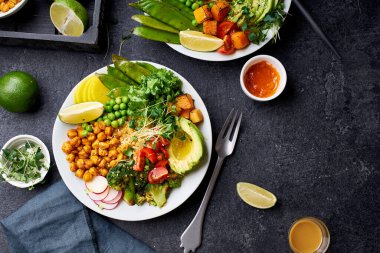 Healthy vegetarian lunch bowls with avocado and chickpeas with quinoa and vegetables garnished with microgreens and nut dressing  on dark concrete background clipart