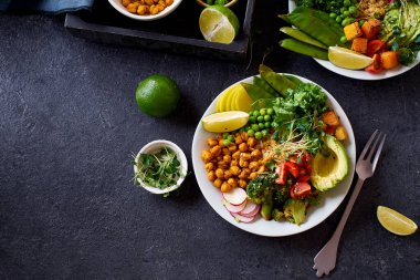 Avokado ve nohutlu sağlıklı vejetaryen yemek kâseleri kinoa ve sebzelerle bezenmiş yeşil ve koyu beton arka planda fındık soslu.