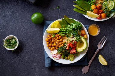 Avokado ve nohutlu sağlıklı vejetaryen yemek kâseleri kinoa ve sebzelerle bezenmiş yeşil ve koyu beton arka planda fındık soslu.