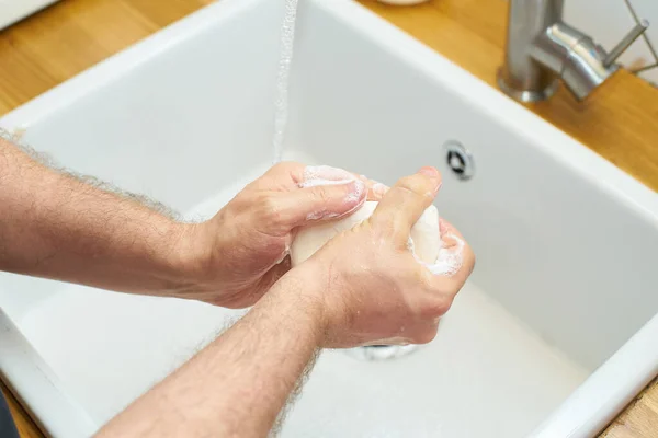 Man washing hands with soap by kitchen sink, preventing virus spread and personal hygiene concept