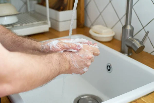 Man washing hands with soap by kitchen sink, preventing virus spread and personal hygiene concept