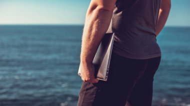 bir dizüstü bilgisayar deniz arka plan üzerinde tutan adam