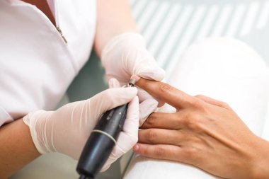 Güzellik salonundaki donanım manikürünü yakından çek. Manikürcü kadın parmaklarına manikür yapmak için elektrikli tırnak matkabı uyguluyor..