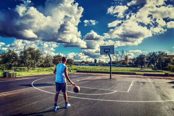 Баскетболист на детской площадке под драматическим небом — стоковое фото