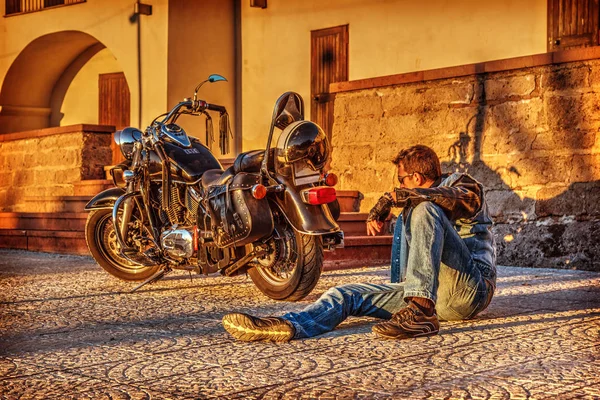 Człowiek siedzi przez klasyczny motocykl o zmierzchu — Zdjęcie stockowe