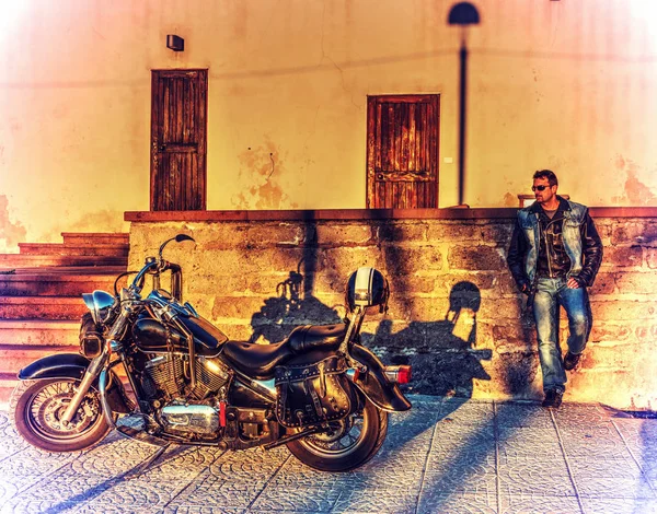 Biker standing by a classic motorycle at sunset — Stock Photo, Image