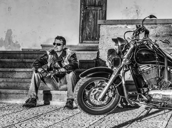 Homem sentado por uma motocicleta clássica em preto e branco — Fotografia de Stock