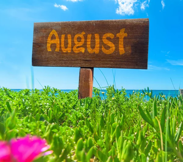 Agosto scritto su un cartello di legno su un campo verde — Foto Stock