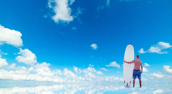 Surfer with his surfboard standing on the water under a cloudy s — 스톡 사진