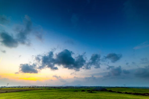 Dark clouds over a green field at sunset