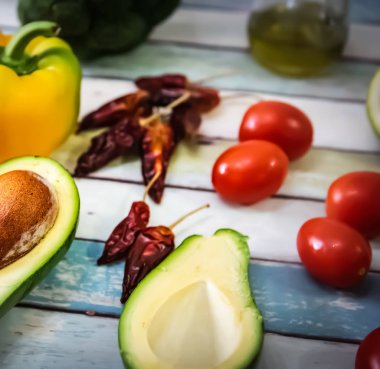 Avokado, domates ve diğer sebzeler ahşap bir masada.