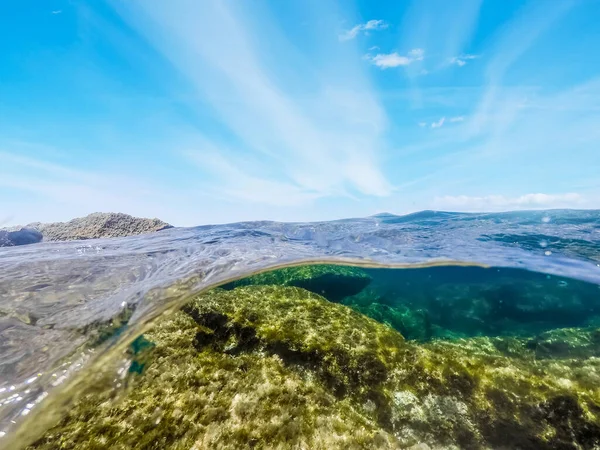 Rocks and blue sky in split underwater view. Alghero, Italy