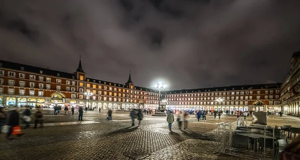 People in Plaza Mayor under a cloudy sky at night. Madrid, Spain