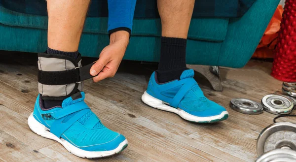 Close up of a man closing velcro strap of an ankle weight during a home workout