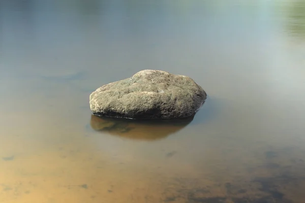 Hladký balvan leží v klidné vodě — Stock fotografie