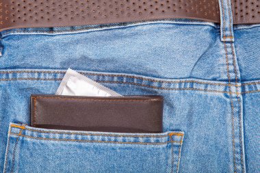 Kahverengi cüzdan ve gri prezervatif kot pantolonun cebine.