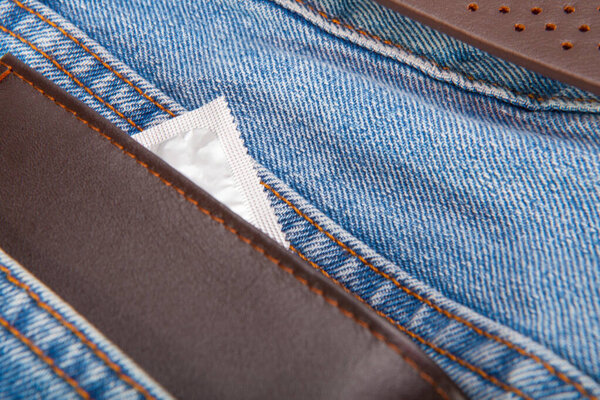Brown wallet and grey condom put in the blue jeans pocket