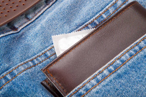 Brown wallet and grey condom put in the blue jeans pocket