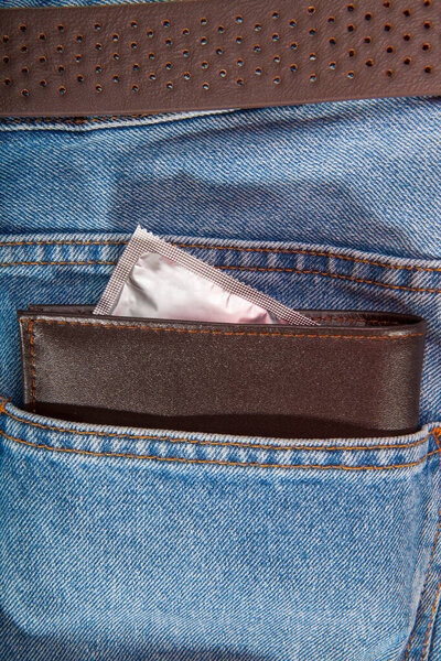 Brown wallet and grey condom put in the blue jeans pocket