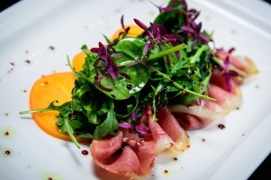 Kızarmış domuz pastırması otlar ve siyah arka plan beyaz tabak turuncu meyve salatası