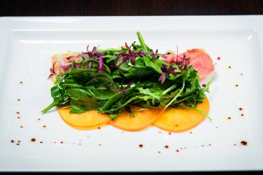 Kızarmış domuz pastırması otlar ve siyah arka plan beyaz tabak turuncu meyve salatası