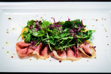 Kızarmış domuz pastırması otlar ve siyah arka plan beyaz tabak turuncu meyve salatası