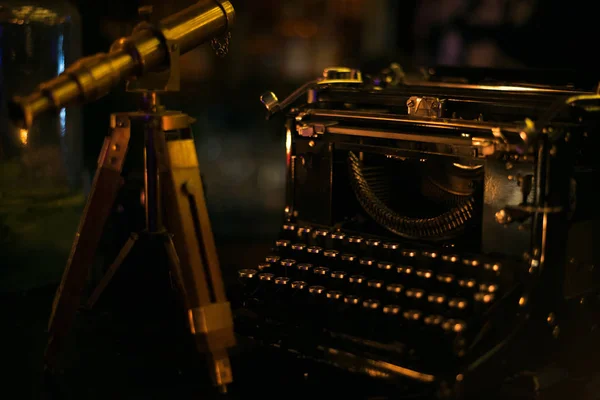 Small vintage telescope standing on the wooden table next to old dark typewriter — Stock Photo, Image