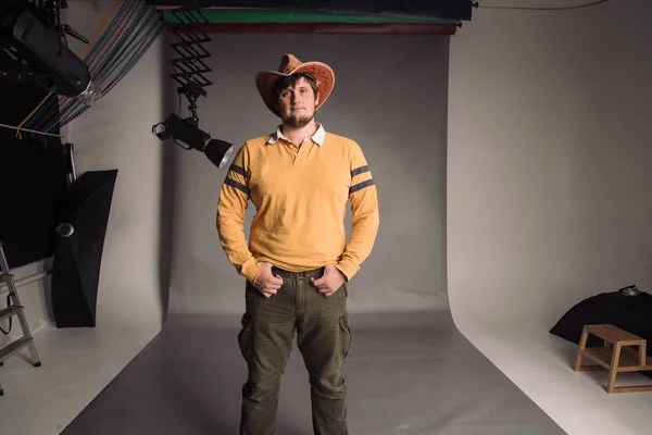 Portrait of big man in a cowboy hat and a yellow shirt. Young man. The studio shot in the gray wall.