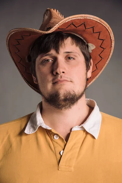 Portrét velký muž v kovbojském klobouku a žlutou košili. Mladý muž. Studio v šedé zdi. Neutrální výraz obličeje — Stock fotografie