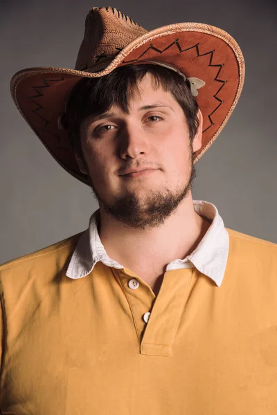 Portret van de grote man in een cowboy hoed en een gele overhemd. Smail Young man. De studio opname in de grijze muur. — Stockfoto