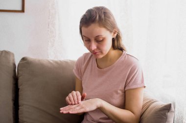 Bir krem cildi kaydetmek için ellerini uygulayarak evde, kanepede oturan çekici genç kadın portresi