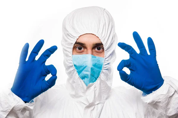 Portrait de jeune homme en uniforme médical blanc protecteur donnant signe OK pendant la pandémie de coronavirus. Épidémie, pandémie de coronavirus covide 19 . — Photo