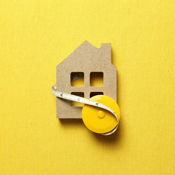 House model with tape measure on yellow fabric background. Buying a house, house size, real estate concept