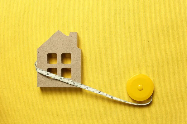 House model with tape measure on yellow fabric background. Buying a house, house size, real estate concept