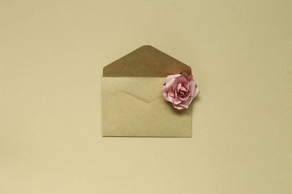 Sobre de papel marrón kraft con rosa sobre fondo marrón — Foto de Stock