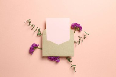Kraft zarfı ve üzerinde çiçek olan boş bir kart. Pembe arka planda okaliptüs yaprakları. Çiçek kompozisyonu, düz konum, üst görünüm, kopyalama alanı