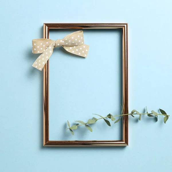 Empty photo frame with eucalyptus leaves and ribbon on sky blue background. top view, copy space