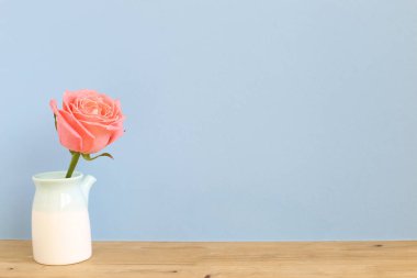 Pastel mavi arka planlı ahşap masada pembe bir gül. Boşluğu kopyala