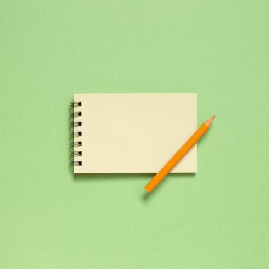 Pastel yeşil arka planda renkli kalemli boş not defteri. Üst görünüm, boşluk kopyala