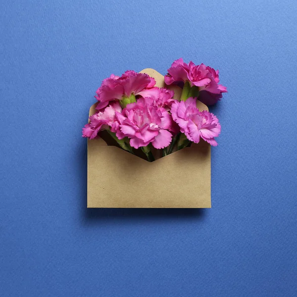 Pink spray carnation flowers in kraft envelope on dark blue background. Floral composition, flat lay, top view, copy space